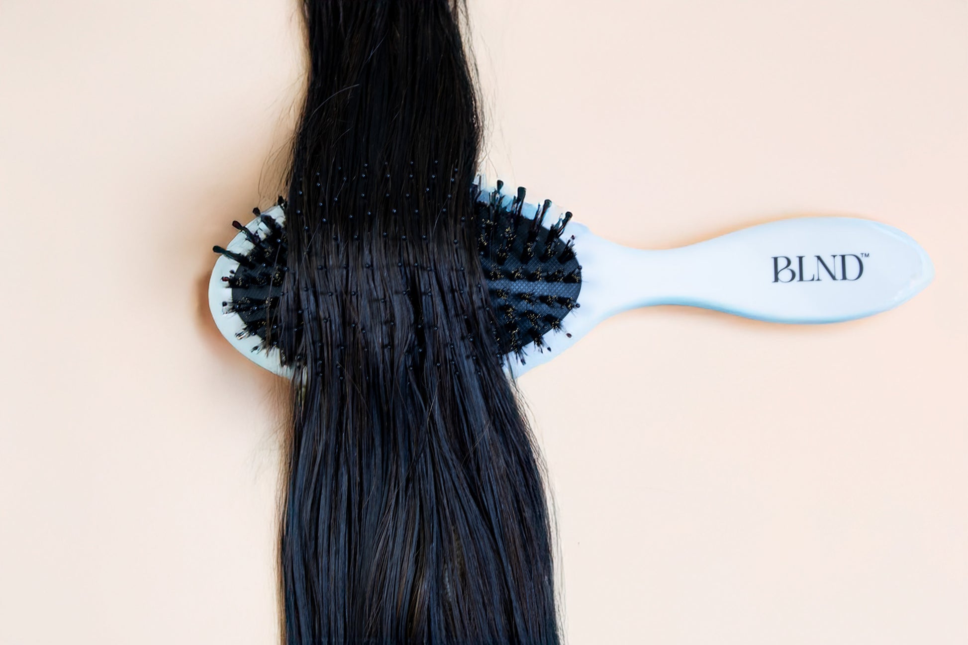 Person using a cream hairbrush on long black hair against a beige background