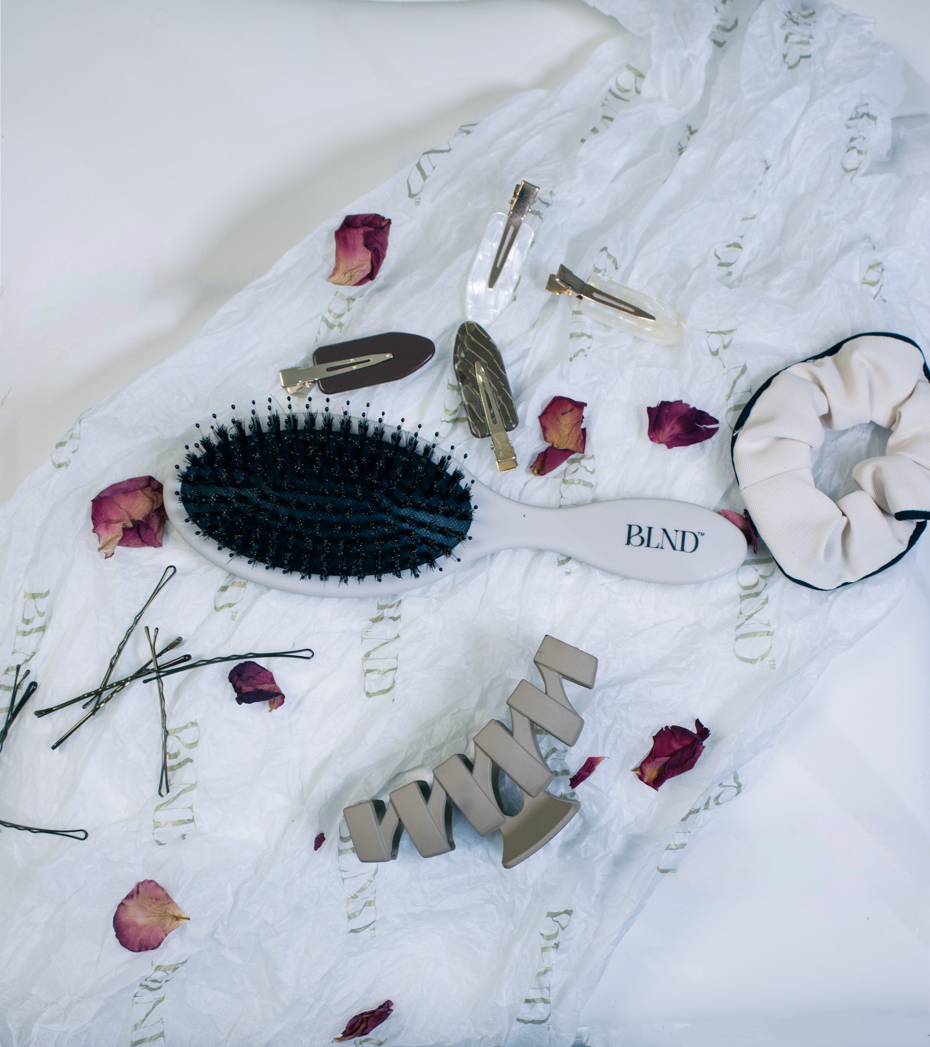 Hairbrush, hair clips, and scrunchie on a textured white fabric background with decorative elements.