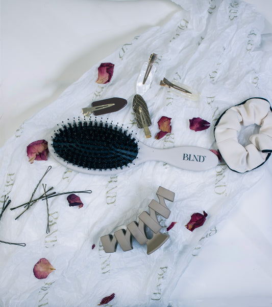 Hairbrush, hair clips, and scrunchie on a textured white fabric background with decorative elements.